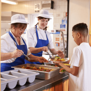 Child getting served food in a cafeteria with two lunch ladies